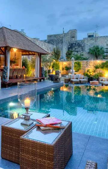 Luxury outdoor living space designed by Aces Design Studio in Gżira, Malta, featuring a modern swimming pool, landscaped garden, elegant outdoor seating, ambient lighting, contemporary villa architecture, and premium exterior design.